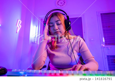 Game over. Angry Asian gamer wearing gaming headphones playing video game on computer PC with purple light on night at home, female tired feeling sad disappointed about game losing, player Game over. Angry Asian gamer wearing gaming headphones playing video game on computer PC with purple light on night at home, female tired feeling sad disappointed about game losing, player 141816791