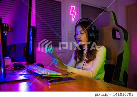Young Asian woman gamer wearing headphones playing video game on modern gaming pc computer have long time she wrist pain, female broadcast streaming plays online home games Young Asian woman gamer wearing headphones playing video game on modern gaming pc computer have long time she wrist pain, female broadcast streaming plays online home games 141816798