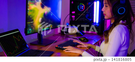 Asian professional gamer playing online video game on desktop computer PC screen display have colorful neon LED lights, young woman in gaming headphones using computer for playing game Asian professional gamer playing online video game on desktop computer PC screen display have colorful neon LED lights, young woman in gaming headphones using computer for playing game 141816805