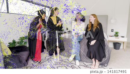 Celebrating four grads wearing gowns in modern bedroom with bed, mortarboard, yellow stole, phone 141817491