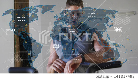 Checking smartwatch, man wearing sleeveless hoodie leaning on spin bike in home gym, map overlay Checking smartwatch, man wearing sleeveless hoodie leaning on spin bike in home gym, map overlay 141817498