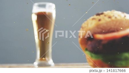 Displaying seeded hamburger at right on wooden tabletop, with tall glass and gold stars, copy space Displaying seeded hamburger at right on wooden tabletop, with tall glass and gold stars, copy space 141817666