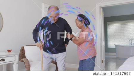 Senior woman supporting partner using wooden cane in bedroom, wearing pink top, jeans, smartwatch 141817697