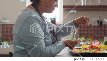 Sprinkling woman in apron seasoning vegetables on tray in kitchen with digital overlay, copy space Sprinkling woman in apron seasoning vegetables on tray in kitchen with digital overlay, copy space 141817714