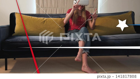 Holding white VR headset, red-tee woman in cuffed jeans gesturing on living-room sofa with overlays Holding white VR headset, red-tee woman in cuffed jeans gesturing on living-room sofa with overlays 141817808