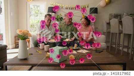 Three relatives celebrating birthday in living room, holding cake, gift, pink party hat, AR overlay 141817902