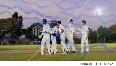 Standing five players in whites exchanging handshakes on grass pitch at dusk, with bats and helmets 141818252