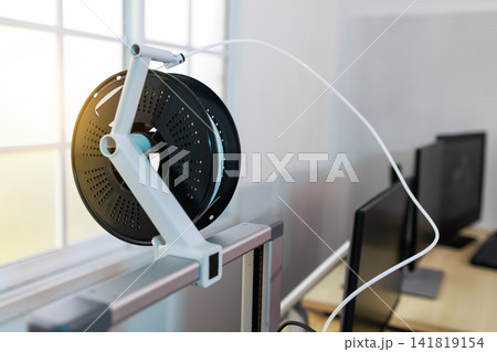 3d printer filament spool mounted on a frame near a window with office computers in the background. 3d printer filament spool mounted on a frame near a window with office computers in the background. 141819154
