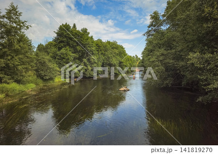 Scenic summer landscape of a calm river in a dense green forest with people enjoying stand up paddleboarding (SUP) activity. Scenic summer landscape of a calm river in a dense green forest with people enjoying stand up paddleboarding (SUP) activity. 141819270