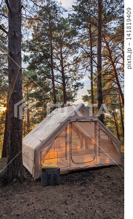 Glamping tent glowing at sunset among tall pine trees inside quiet forest campsite, warm interior light, soft sky behind branches, rustic outdoor retreat in nature Glamping tent glowing at sunset among tall pine trees inside quiet forest campsite, warm interior light, soft sky behind branches, rustic outdoor retreat in nature 141819409