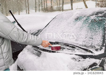 Man in gloves brushing deep snow from car windshield wiper blades 141820043