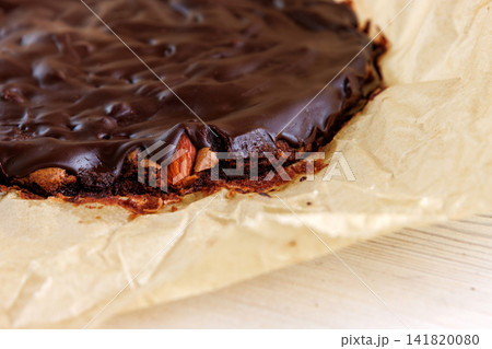 Closeup of freshly baked chocolate brownie with a glossy top and dense fudgy edge on parchment paper. Closeup of freshly baked chocolate brownie with a glossy top and dense fudgy edge on parchment paper. 141820080