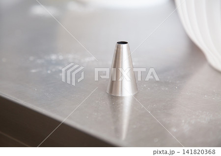 Minimalist stainless steel cone standing on brushed metal surface with soft bright reflections and shallow depth of field, creating clean industrial texture and abstract modern composition 141820368