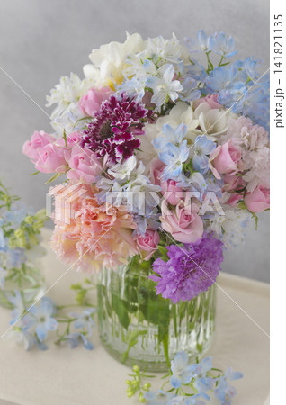 ガラス花瓶に飾られた淡いピンクと水色の華やかなフラワーブーケ 141821135
