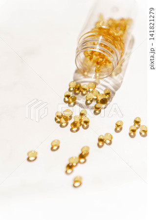 Golden softgel supplement capsules spilling from a transparent bottle Golden softgel supplement capsules spilling from a transparent bottle 141821279