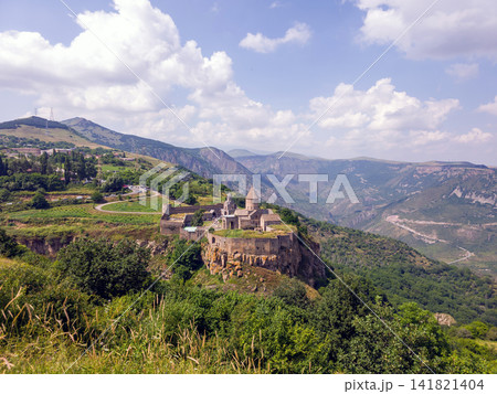 Monastery ruins atop steep hill with surrounding forested mountains 141821404