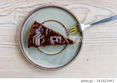 Overhead view of a triangular slice of homemade chocolate almond brownie served on a ceramic plate with a fork on a light wooden table. Overhead view of a triangular slice of homemade chocolate almond brownie served on a ceramic plate with a fork on a light wooden table. 141821441