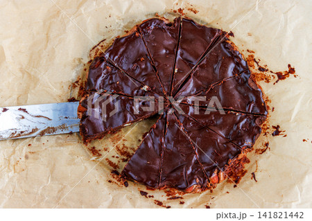 Top view of a homemade chocolate almond brownie cut into triangular portions on parchment paper and a kitchen knife beside. Top view of a homemade chocolate almond brownie cut into triangular portions on parchment paper and a kitchen knife beside. 141821442