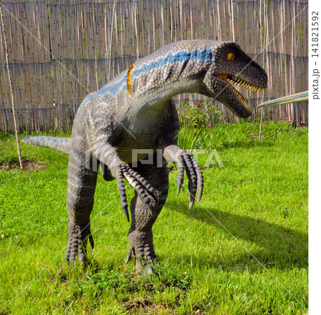 Dinosaur statue poses in grass near wooden fence Dinosaur statue poses in grass near wooden fence 141821592