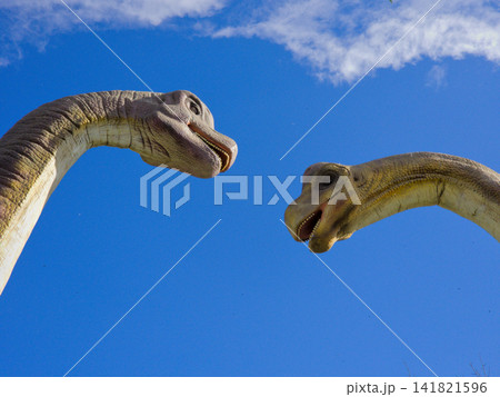 Sauropod dinosaur head statues against a vivid blue sky with clouds 141821596
