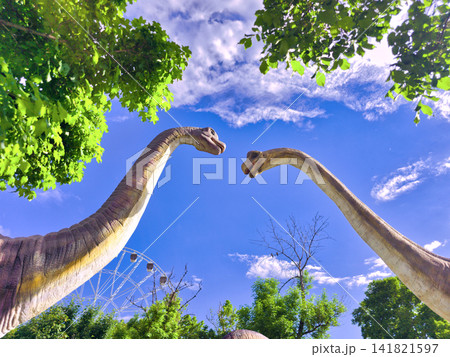 Dinosaur statues in park, trees above, blue sky background Dinosaur statues in park, trees above, blue sky background 141821597