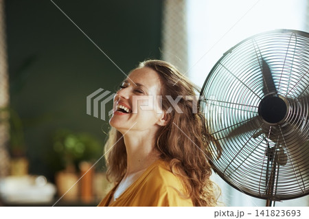 Blissful Woman Enjoying Fan Breeze at Home 141823693