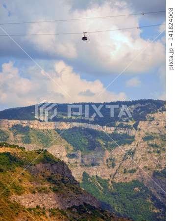 Cable car suspended between mountain peaks under partly cloudy skies Cable car suspended between mountain peaks under partly cloudy skies 141824008