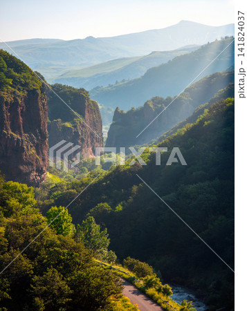 Mountain valley scene with sunlit cliffs, river, and winding path Mountain valley scene with sunlit cliffs, river, and winding path 141824037