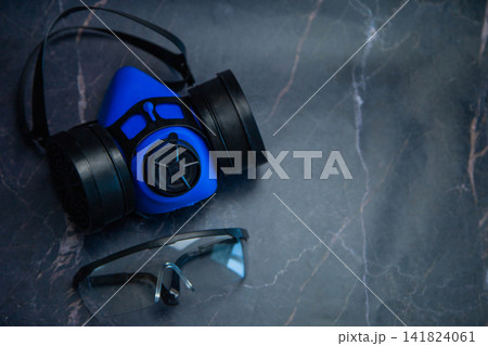 Top view of a blue respirator and goggles placed on a dark marble table with space for text. Concept of personal protective equipment, labor protection, preparation for hazardous work. High quality Top view of a blue respirator and goggles placed on a dark marble table with space for text. Concept of personal protective equipment, labor protection, preparation for hazardous work. High quality 141824061