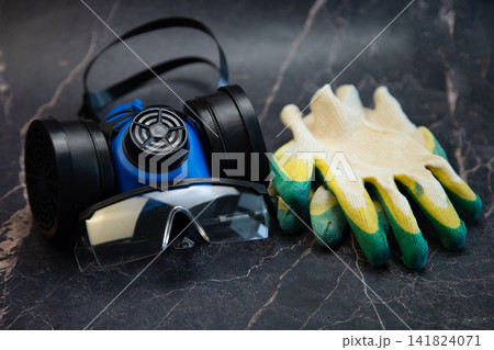 A blue respirator, clear goggles and work gloves are neatly laid out against a dark marble background. Concept, comprehensive employee protection, occupational health and safety, industrial safety 141824071