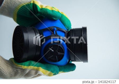 Close-up of hands in construction gloves holding a protective blue mask with two filters on a white background. Concept of personal protective equipment, respiratory protection, repair and 141824117