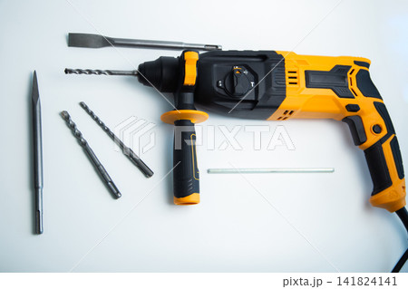 Top view of a yellow and black perforator with a handle, a set of drills, chisels and fasteners on a white background. The concept of a complete set for construction work, universal power tools. High Top view of a yellow and black perforator with a handle, a set of drills, chisels and fasteners on a white background. The concept of a complete set for construction work, universal power tools. High 141824141