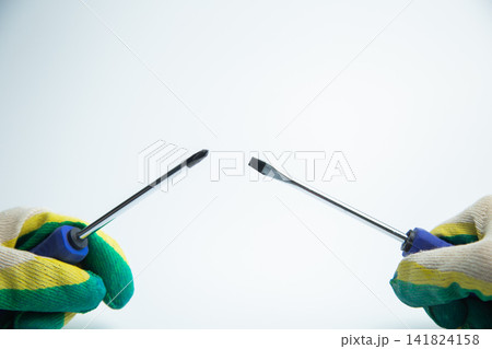 Close-up of two hands in work gloves holding screwdrivers against a white background. Concept of repair, handyman, tools, construction, installation. High quality photo 141824158