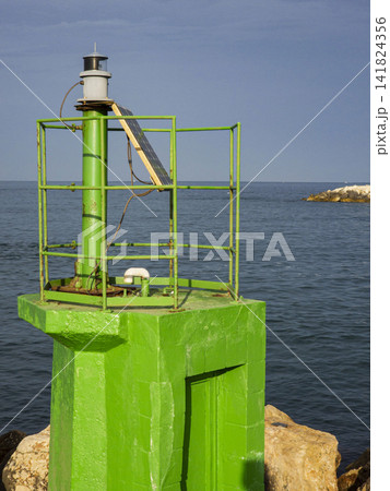 Close up of a green coastal beacon with solar panel on a stone jetty for navigation safety near the water Close up of a green coastal beacon with solar panel on a stone jetty for navigation safety near the water 141824356