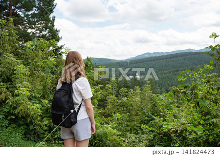 Woman with a backpack enjoying a scenic forest view from a hilltop. 141824473