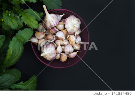 Garlic cloves in a bowl with green leaves nearby Garlic cloves in a bowl with green leaves nearby 141824486