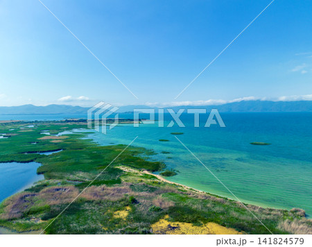 Coastal wetland area with turquoise sea, green vegetation, and distant mountains Coastal wetland area with turquoise sea, green vegetation, and distant mountains 141824579