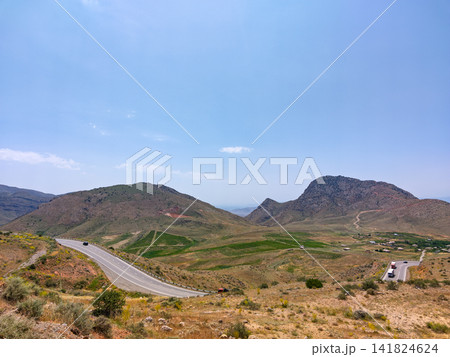 Highway curves across rocky hillsides with distant mountain peaks Highway curves across rocky hillsides with distant mountain peaks 141824624