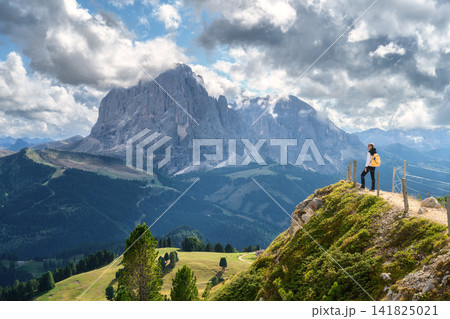 Woman with backpack standing on cliff edge looking at mountains 141825021