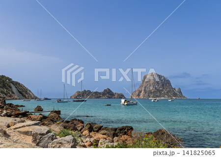 Es Vedra and Es Vedranell off Cala d Hort with anchored sailboats and rocky shoreline. Es Vedra and Es Vedranell off Cala d Hort with anchored sailboats and rocky shoreline. 141825065