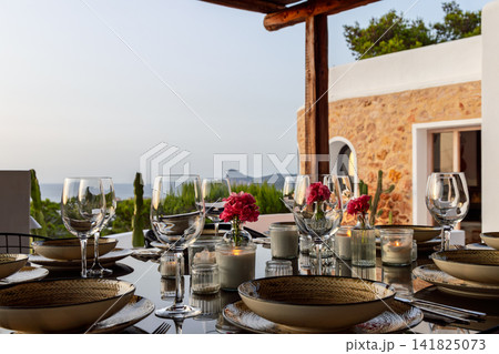 Candlelit table setting on Ibiza, small pink flowers and early candlelight among clear glasses. Candlelit table setting on Ibiza, small pink flowers and early candlelight among clear glasses. 141825073