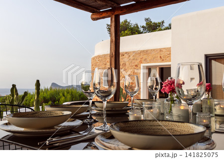 Candlelit place setting in Ibiza, low oblique bowls and glasses beside the illuminated villa. 141825075