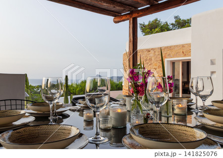 Floral dinner table on Ibiza, symmetrical magenta centerpiece among candles and glassware. 141825076