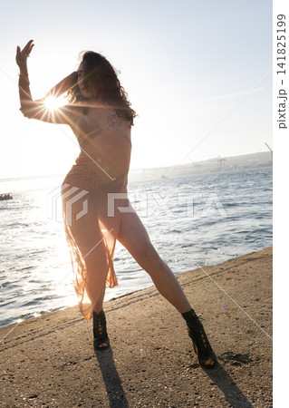 Dancer performs on the shore during sunset with sunlight shining behind Dancer performs on the shore during sunset with sunlight shining behind 141825199