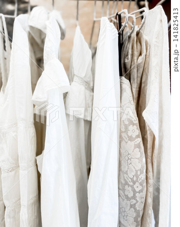 Collection of elegant white and beige garments with delicate lace details hanging on a clothing rack 141825413
