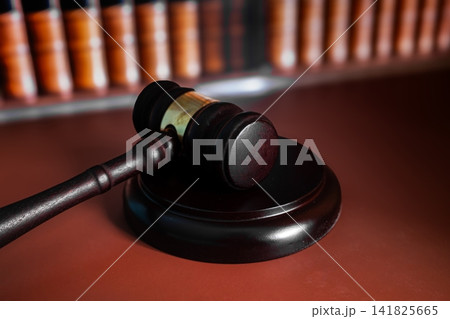 Wooden judge gavel lying beside sound block in front of blurred law books, court justice and legal concept Wooden judge gavel lying beside sound block in front of blurred law books, court justice and legal concept 141825665