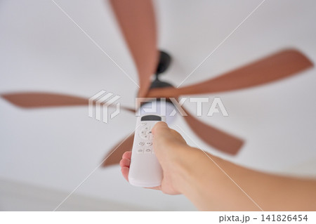 Hand holding remote control aimed at ceiling fan in home interior Hand holding remote control aimed at ceiling fan in home interior 141826454