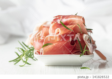 Prosciutto with rosemary on a white wooden table. Prosciutto with rosemary on a white wooden table. 141826522