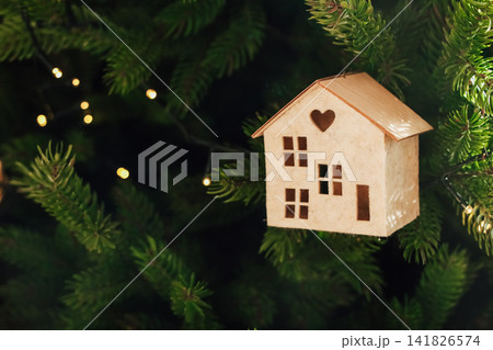 Decorative wooden house ornament hanging on a Christmas tree with warm lights 141826574