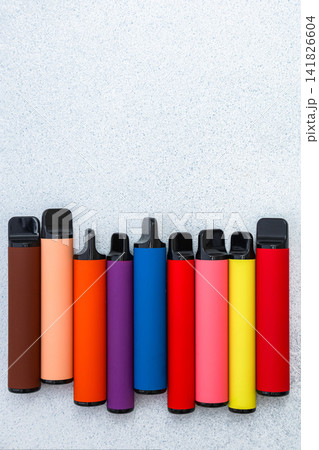 Colorful assortment of electronic cigarettes on a gray background. Variety of modern vaping devices in different colors, minimalistic composition, nicotine alternatives Colorful assortment of electronic cigarettes on a gray background. Variety of modern vaping devices in different colors, minimalistic composition, nicotine alternatives 141826604